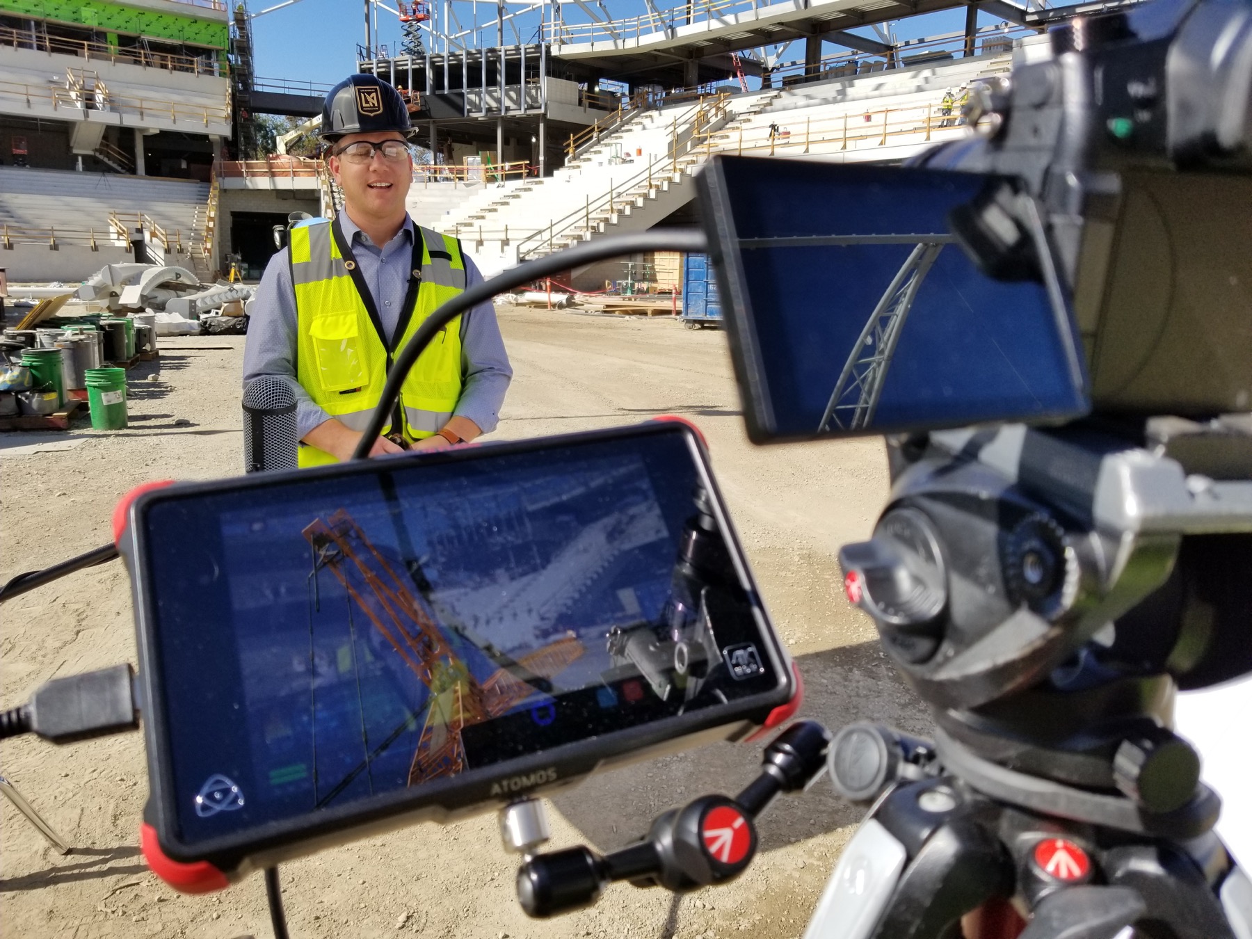 Production camera and external monitor framing an interview at the stadium construction site