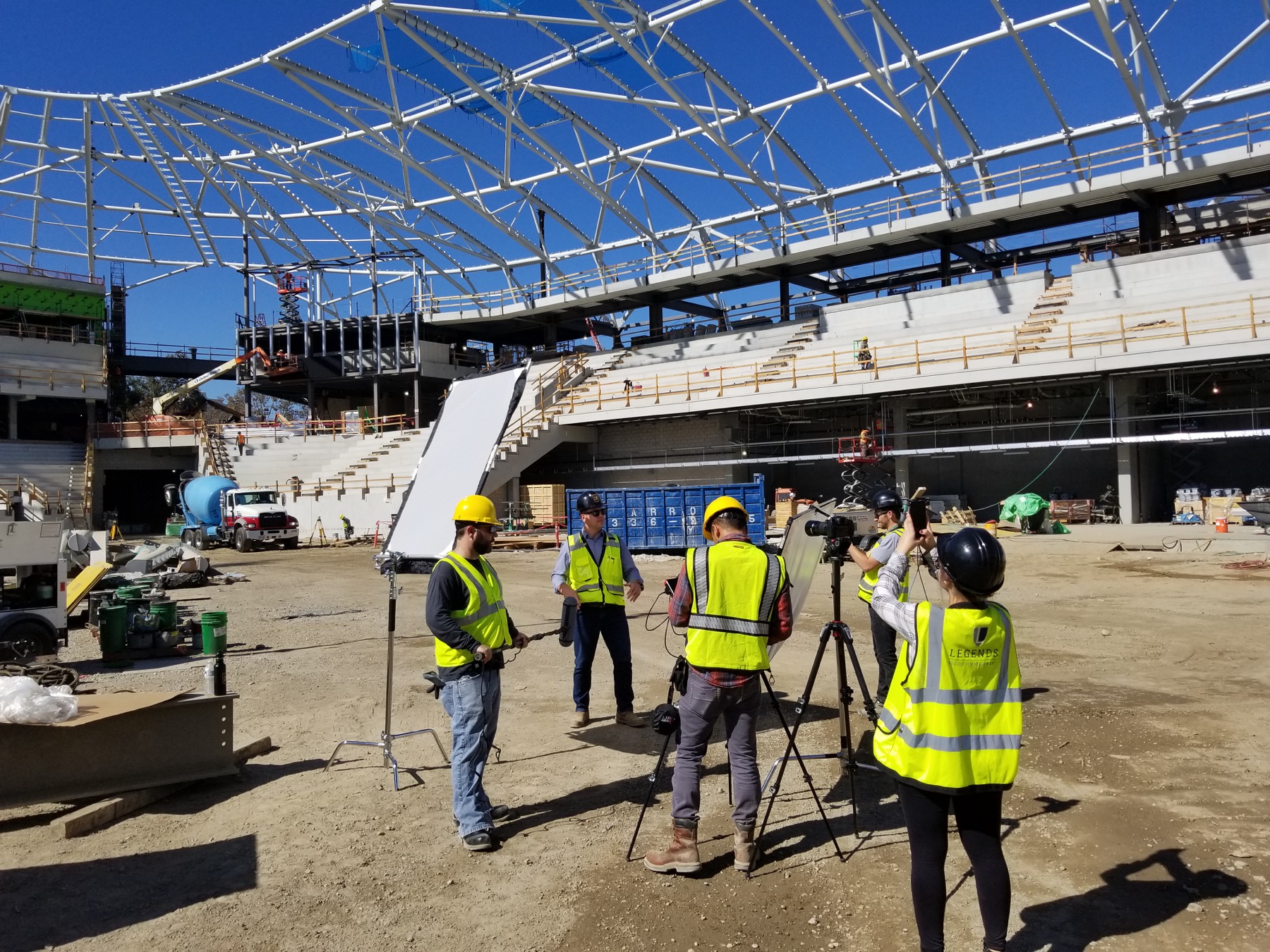 Camera and lighting crew working on the ground inside the stadium’s steel structure