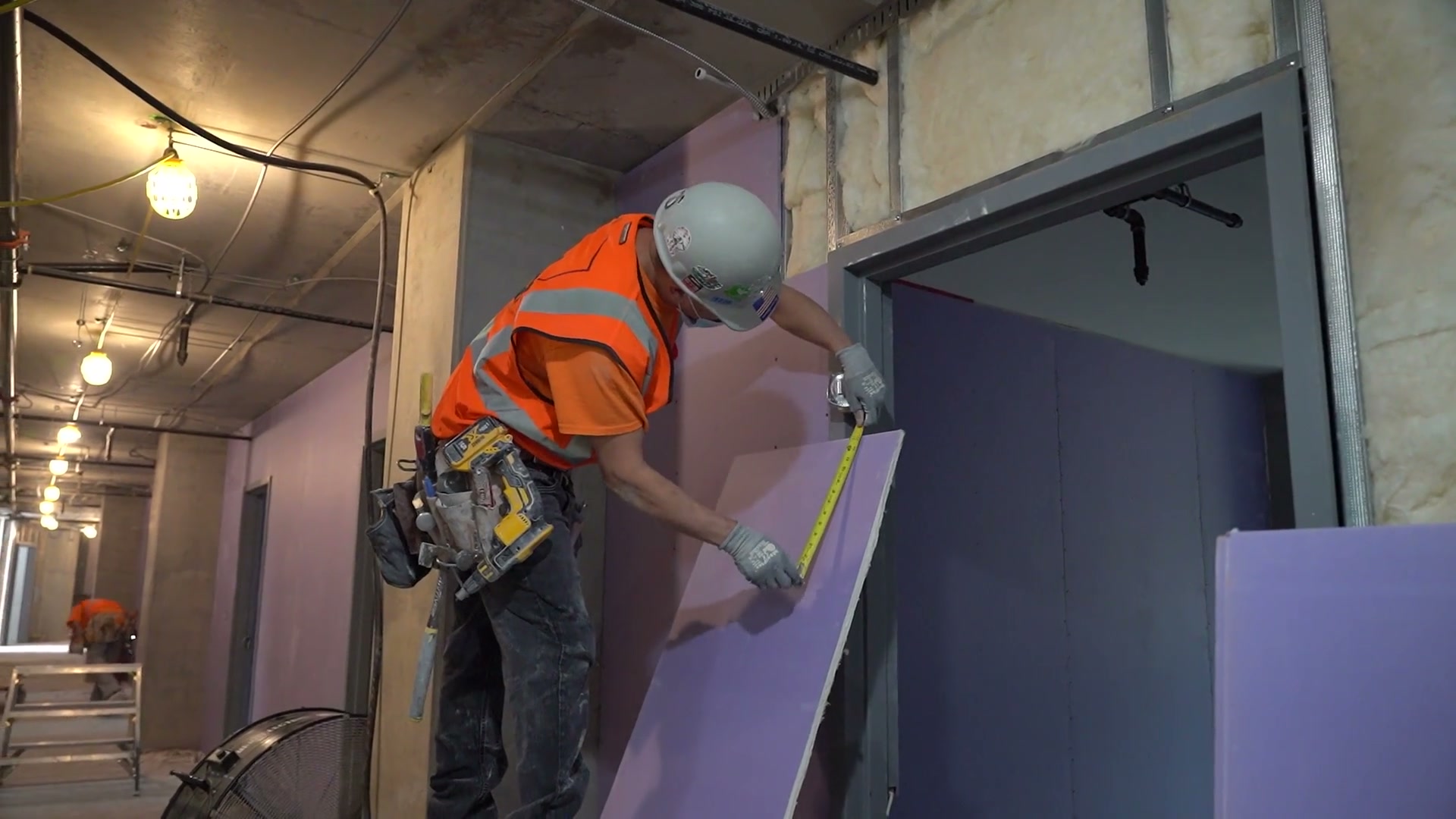 Construction worker measuring drywall in an unfinished interior